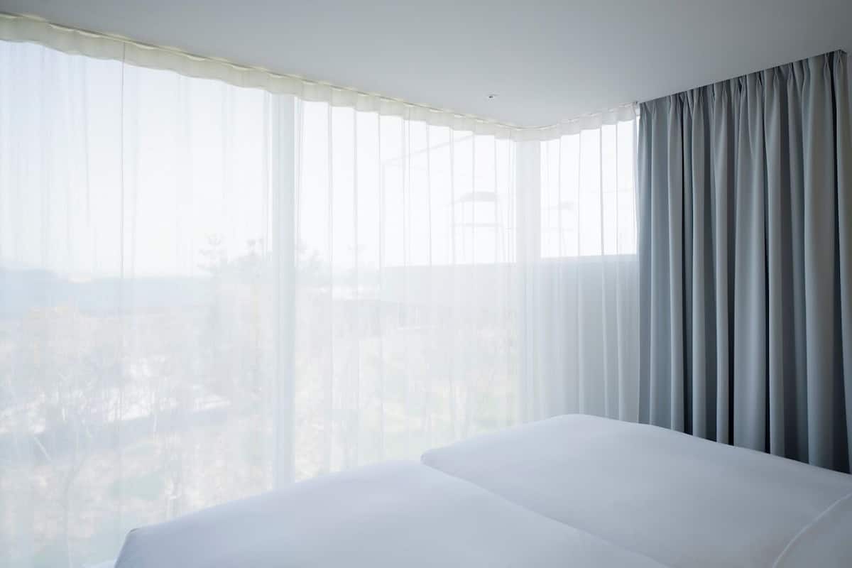A hotel room with a large bed, sheer curtains, and a view of the city.