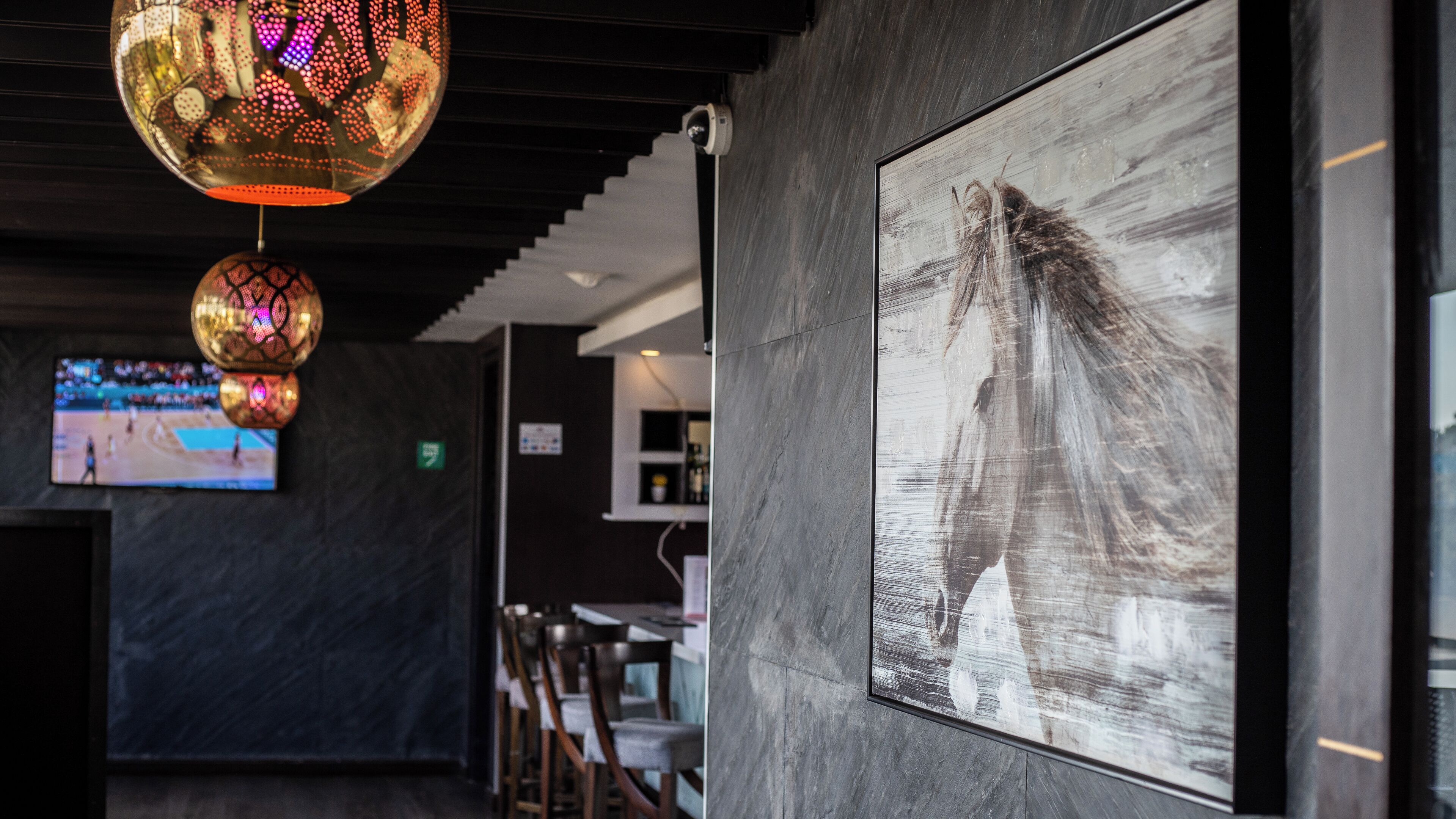 A modern interior with a large abstract painting, a television displaying a sports event, and decorative hanging lights.