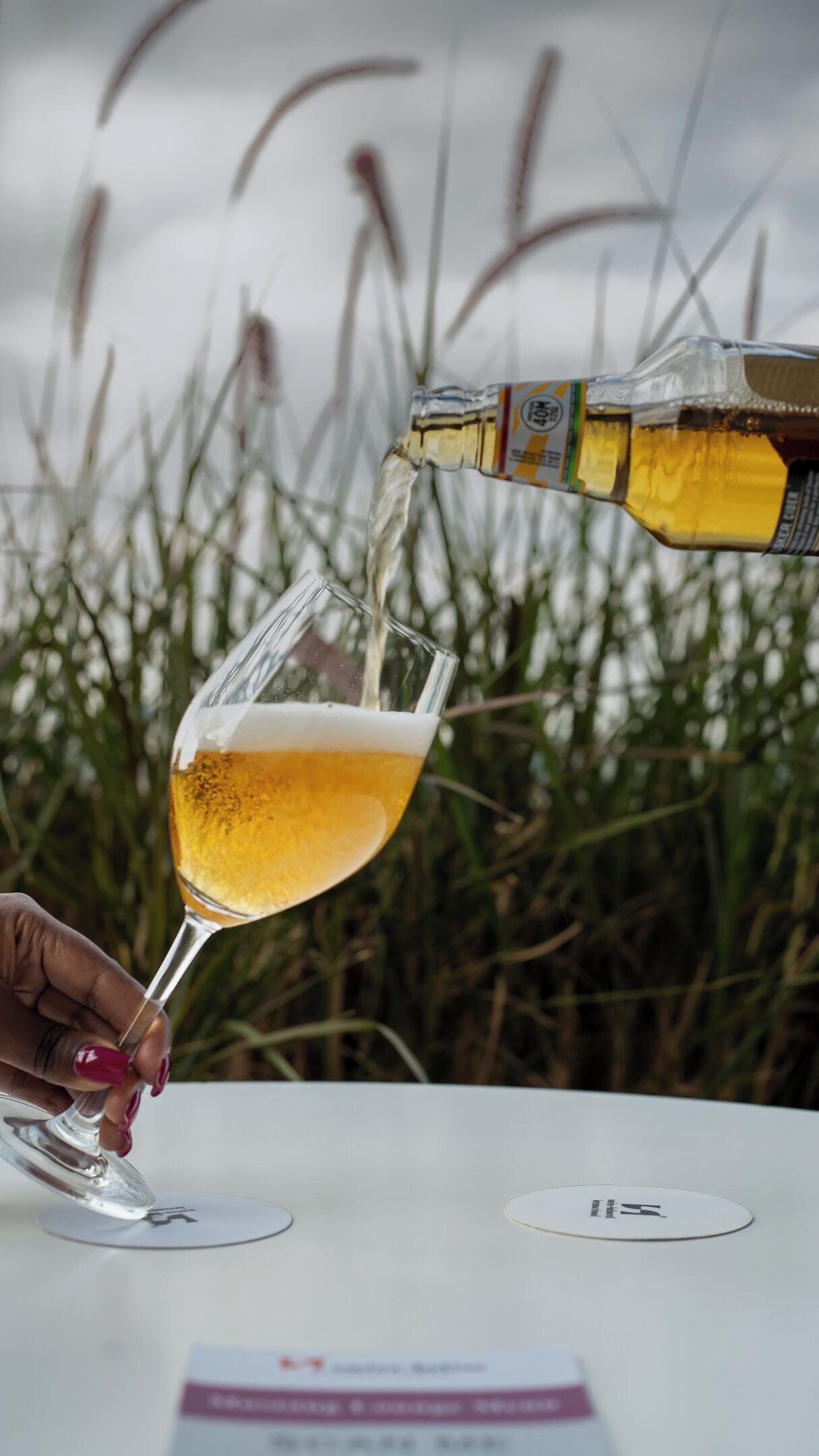 A hand pouring a golden liquid into a glass with a stem.