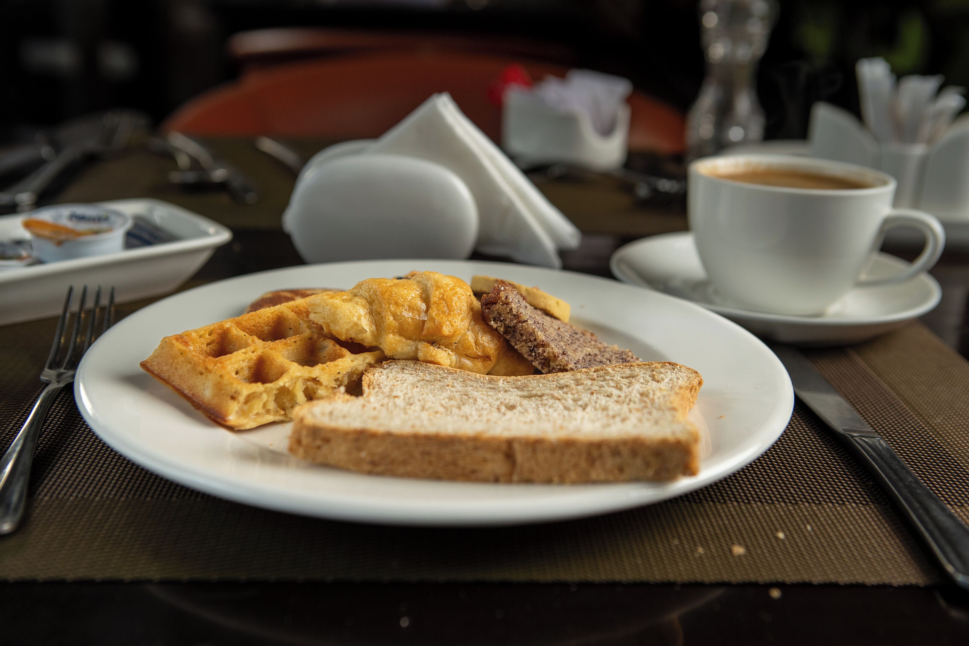 A plate with waffles and toast on a table with a cup of coffee and a salt shaker.