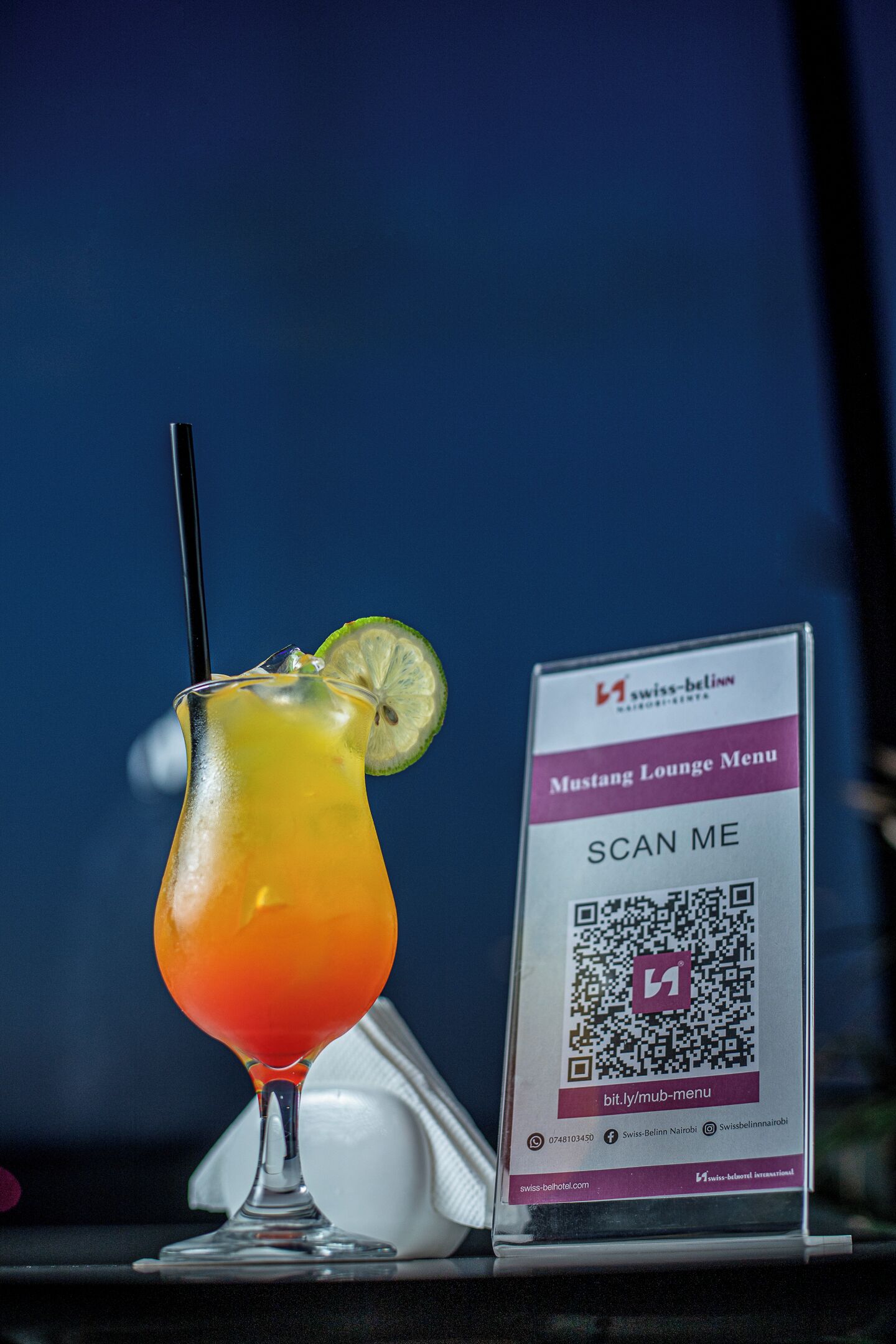 Un cocktail guarnito con una fetta di lime e un menu con codice QR per Swiss-Belmont Nairobi.