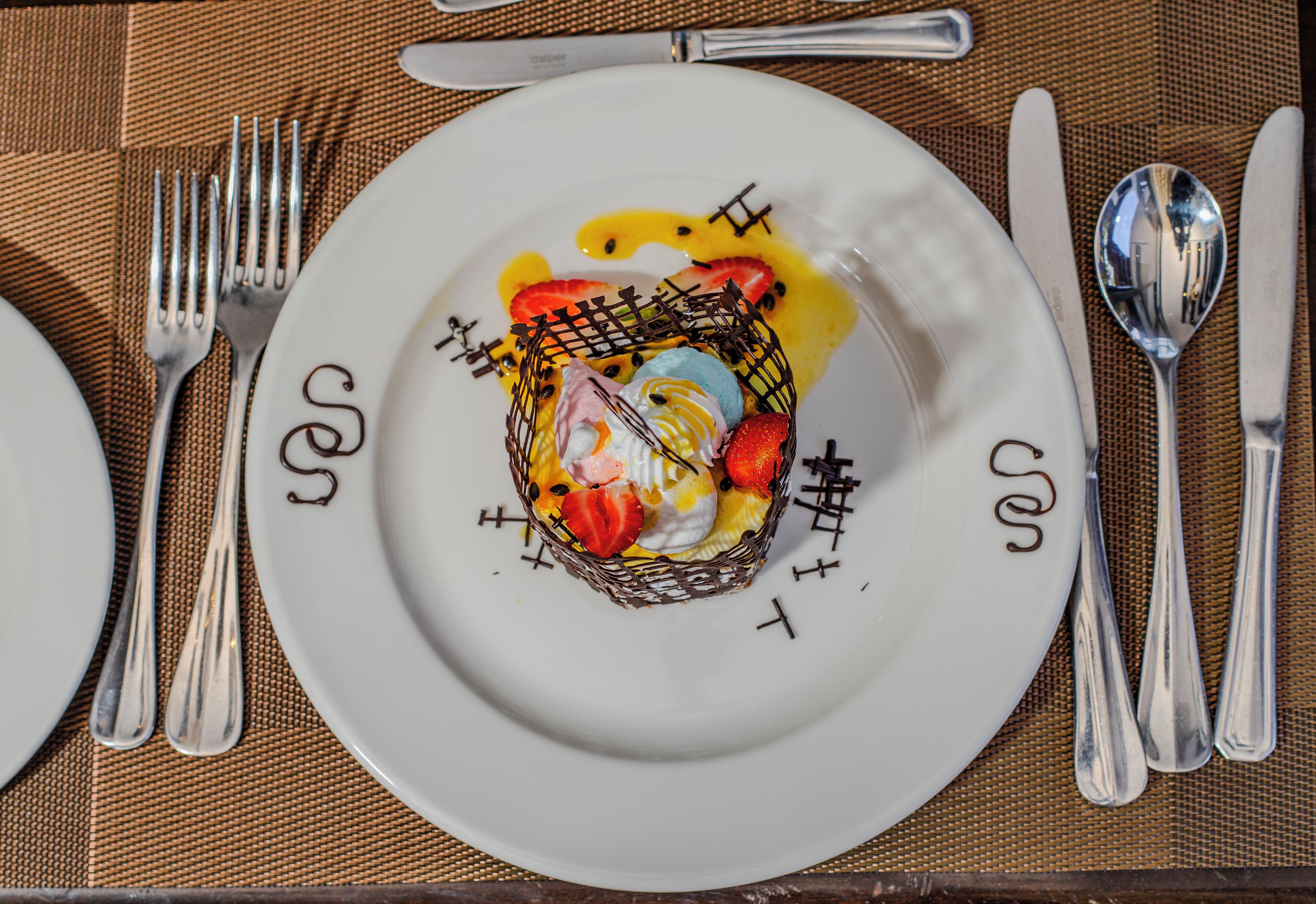 Un postre sobre un plato blanco, con una celosía de chocolate, fresas y salsa amarilla.