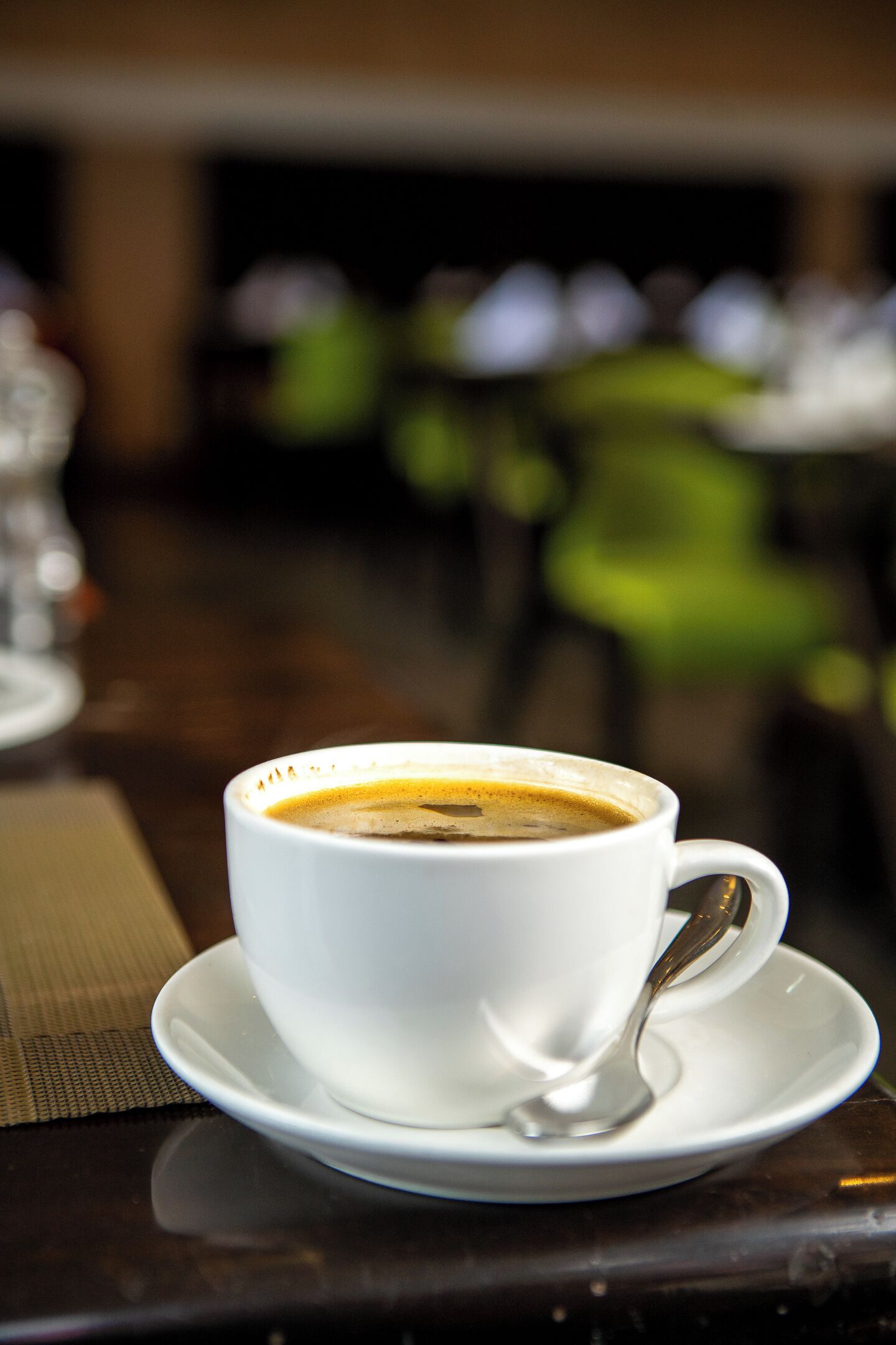 Una taza blanca de café con una cuchara sobre un platito, colocada sobre una mesa con un mantel individual.