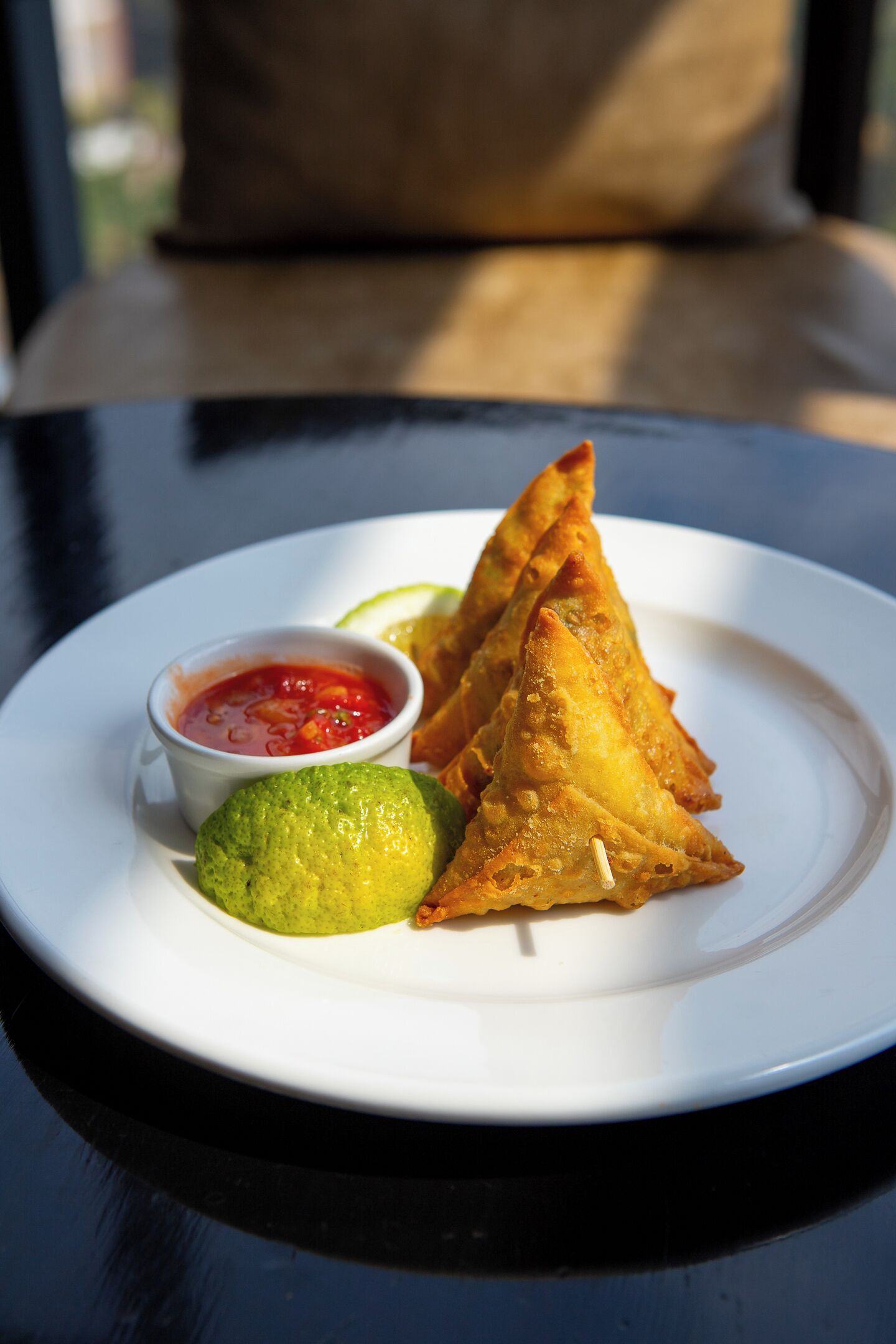 A plate with three samosas, a small bowl of chutney, and a lime wedge on a white plate.