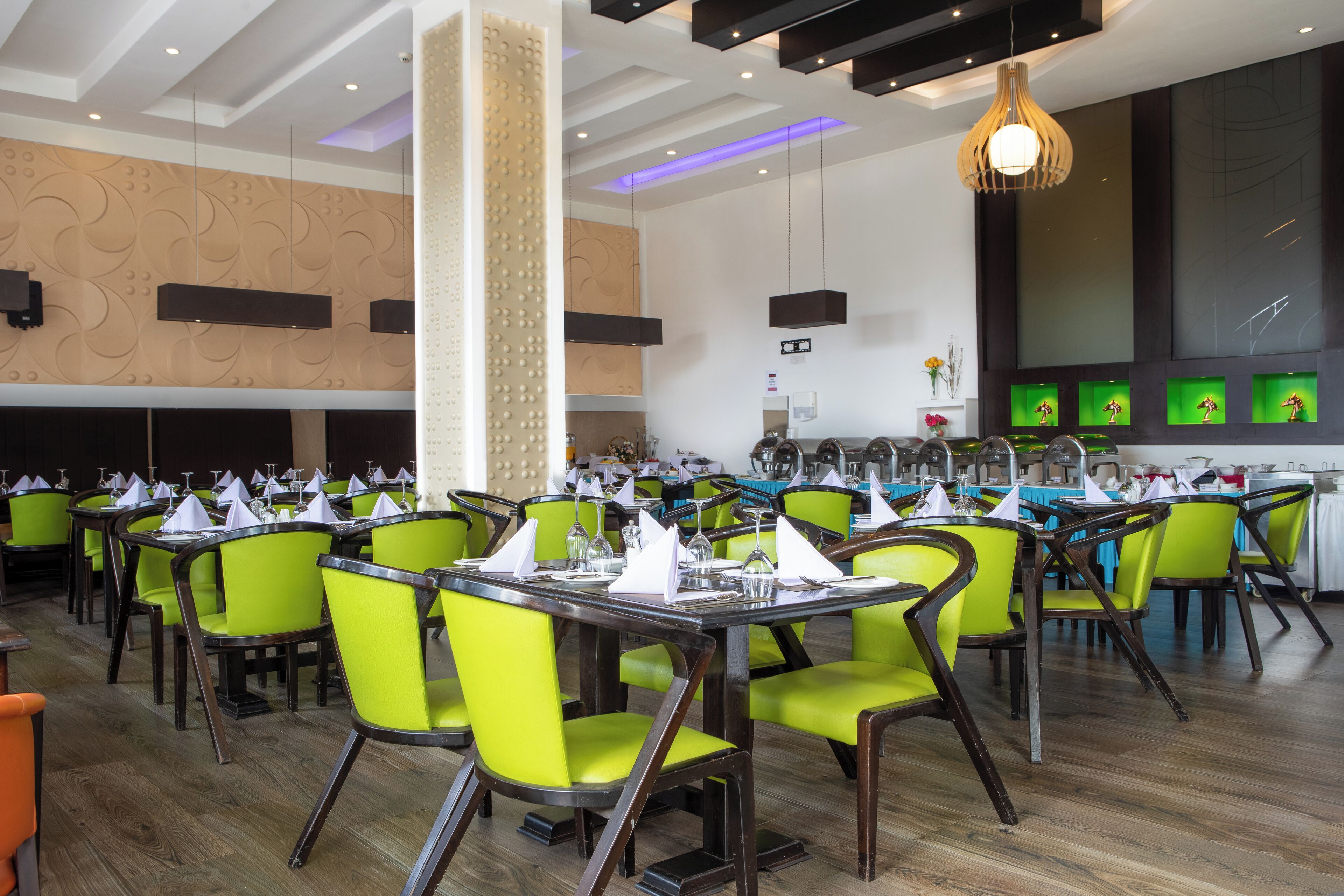 A restaurant with green chairs, wooden tables, and a modern ceiling design.