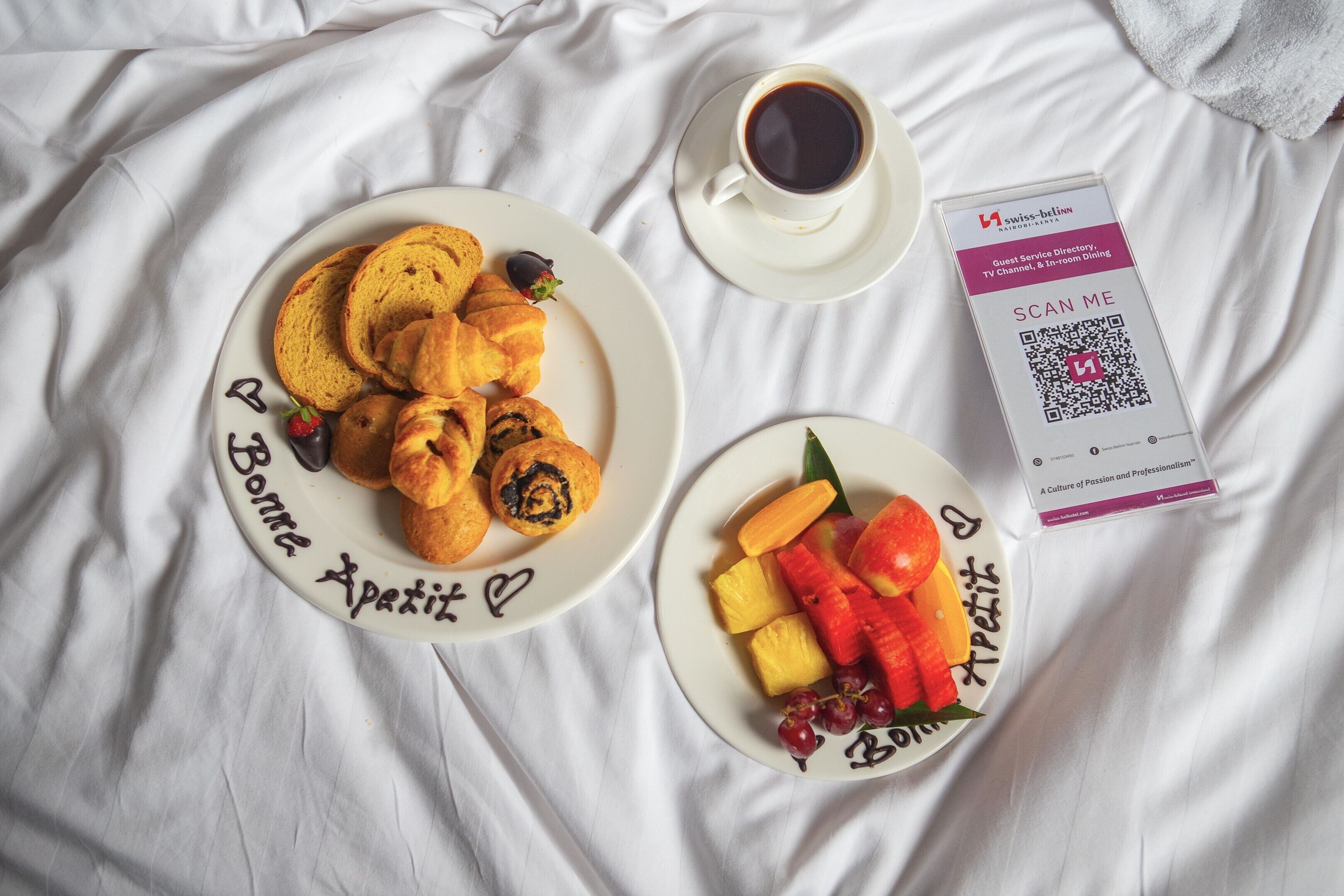 Een ontbijtsetting met croissants, fruit en koffie op een bed.