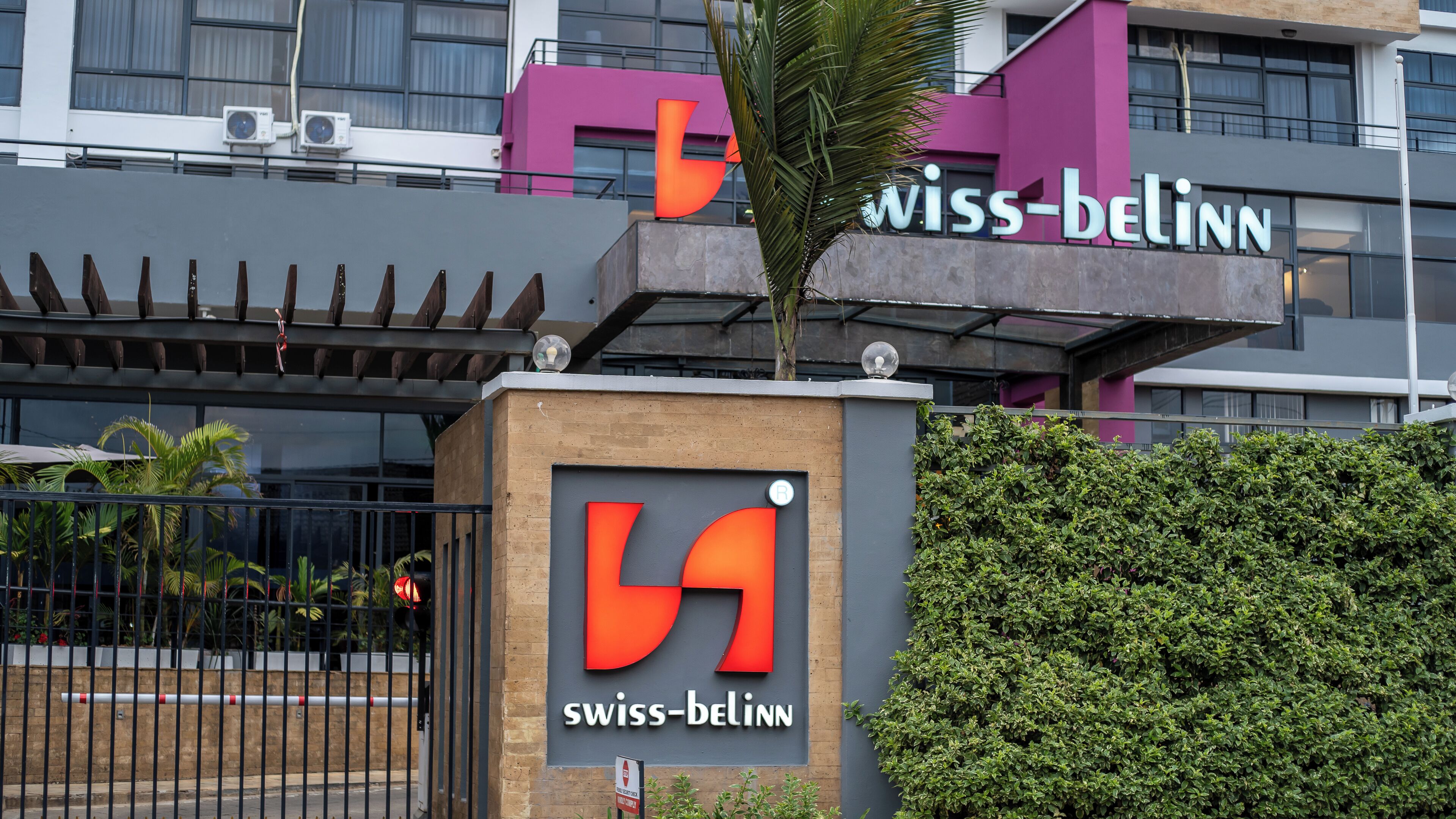 The exterior of a Swiss-Bellinn hotel with a prominent logo, a gated entrance, and a modern building facade.