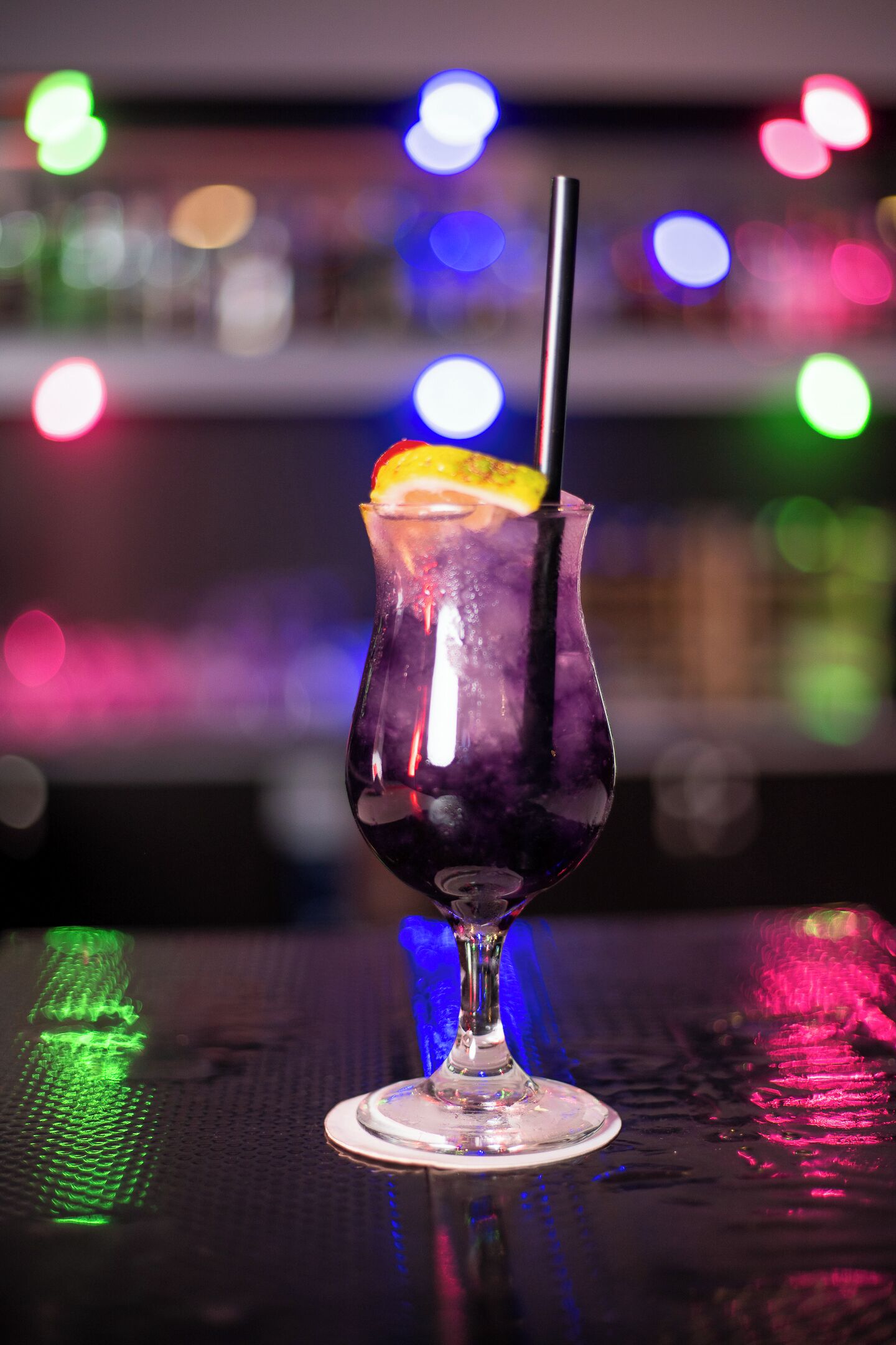 A cocktail glass with a lemon slice and a straw on a reflective surface.