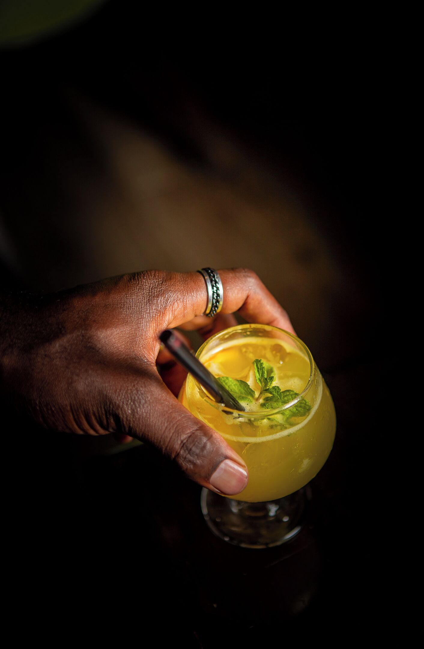 A hand holding a cocktail glass with a lemon slice and mint garnish.