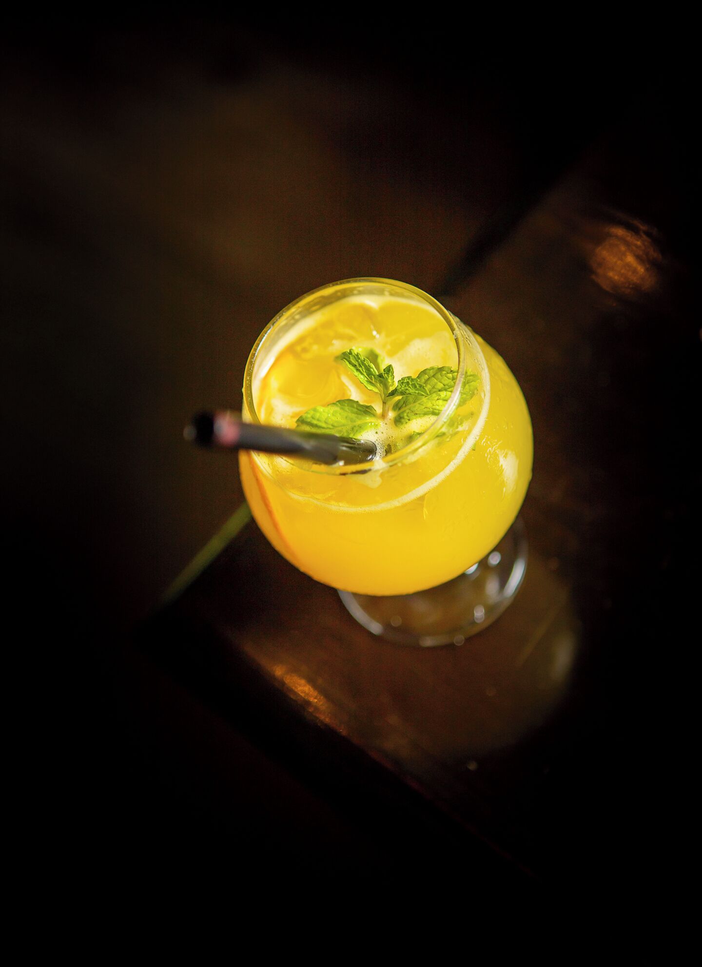 A cocktail with a lemon slice and mint garnish on a dark surface.