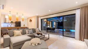 Een moderne woonkamer met een bank, salontafel en eethoek. Achtergrond is een keuken en een schuifdeur die leidt naar een terras buiten met een zwembad.