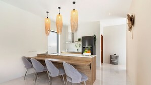 Een moderne keuken met een houten kookeiland, vier grijze stoelen en drie hangende hanglampen.