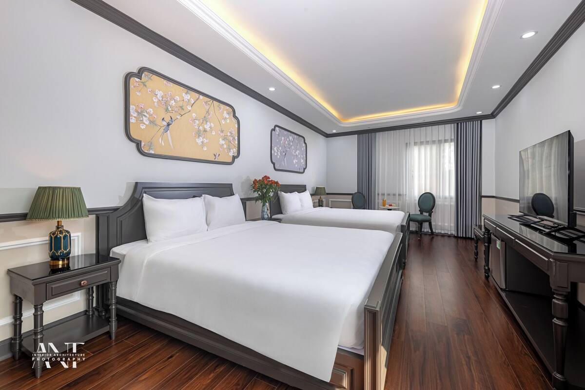 Habitación de hotel moderna con dos camas, televisión de pantalla plana, escritorio y un ventanal con cortinas.