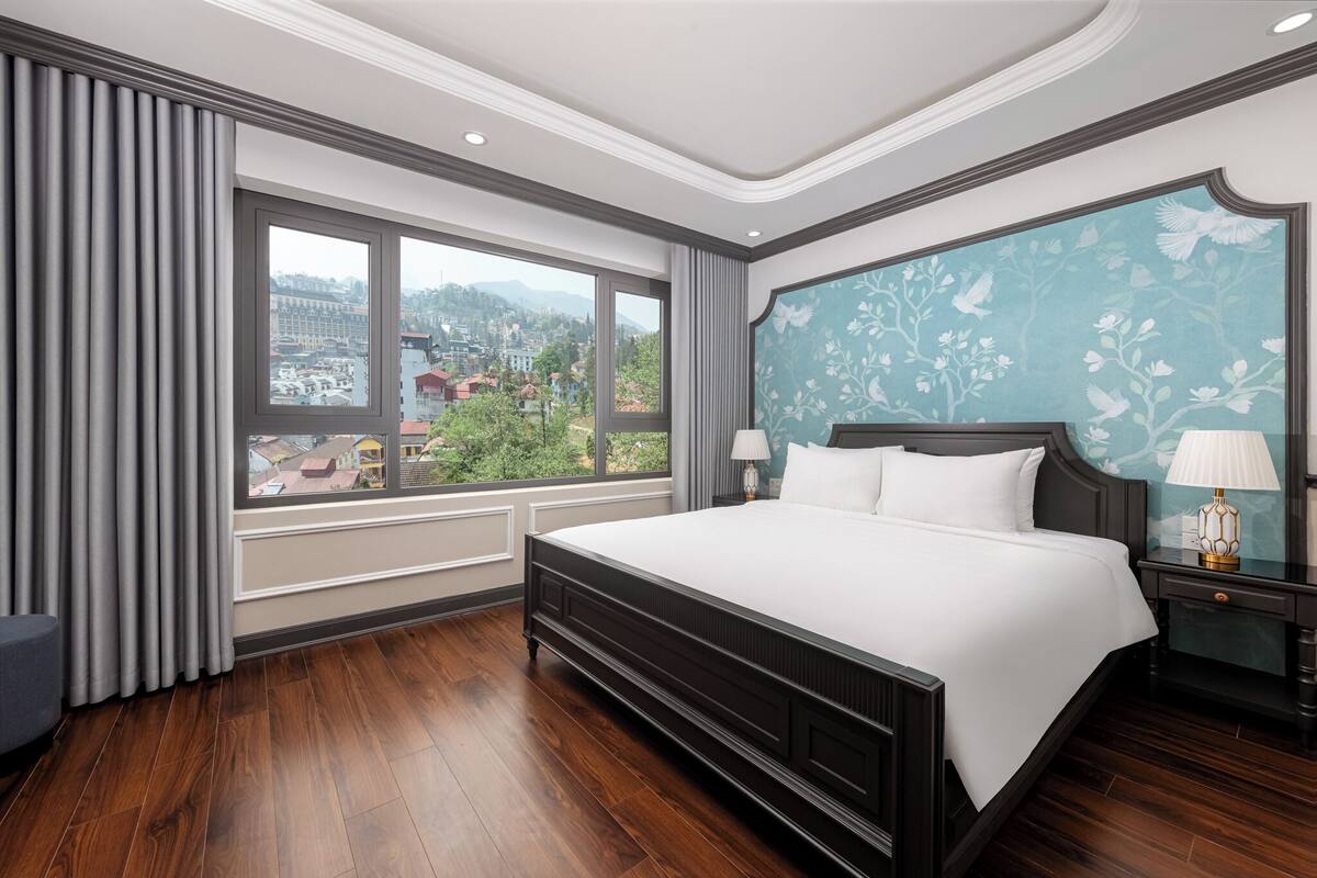 Un dormitorio con una cama grande, vistas a la ciudad y una ventana con cortinas.