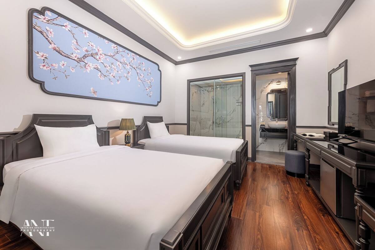 Habitación de hotel con dos camas, una amplia obra de arte de flores de cerezo, un baño moderno con ducha de vidrio y un televisor.