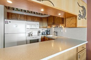 A kitchen with wooden cabinets, a granite countertop, a microwave, a stove, and a coffee maker. - Sunset magic awaits ,1bd Condo with ocean views (Lahaina)