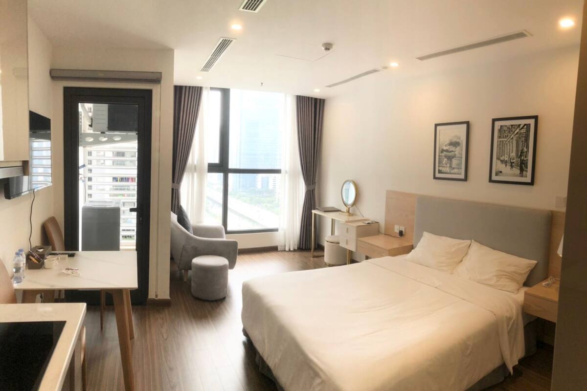 Une chambre d’hôtel comprenant un lit, un bureau, une chaise, une petite table, une table de chevet, un miroir et une fenêtre avec des rideaux.