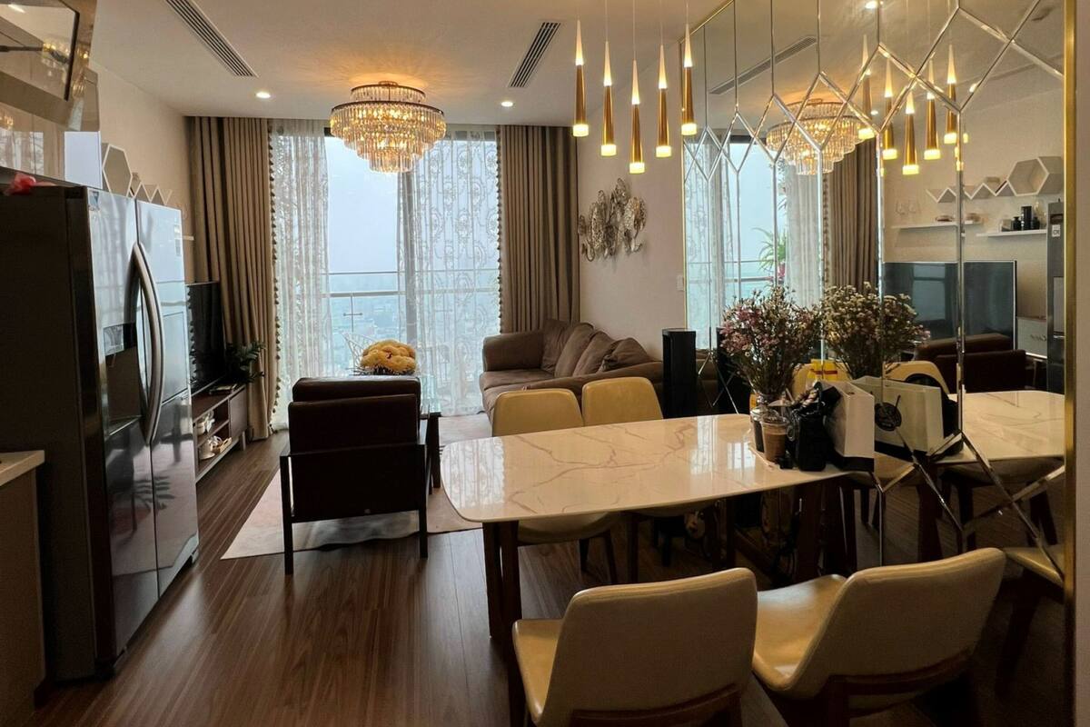 Une cuisine moderne avec un coin repas, dotée d’un plan de travail en marbre, de chaises en bois et de luminaires suspendus.