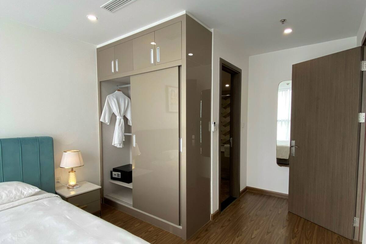 Une chambre d’hôtel moderne avec un lit, une table de chevet avec une lampe, une armoire avec un miroir et un plancher en bois.
