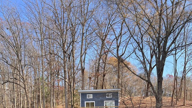 Une maison avec une jetée qui s’avance sur un lac paisible, entourée d’arbres.