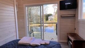 Une chambre avec un grand lit, un téléviseur fixé au mur et une vue sur un étang et des arbres à l’extérieur.