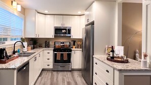 Une cuisine moderne avec des meubles blancs, des appareils électroménagers en acier inoxydable et un plancher en bois.