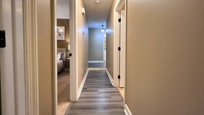 A narrow hallway with a carpeted floor, a bed with a headboard visible on the left, and a door on the right. - NEW! King Bed, Fire Place,  Near ATL W/ Patio (Norcross)