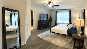 Une chambre à coucher avec un lit à baldaquin, un ventilateur de plafond, un grand miroir, une commode et un téléviseur.