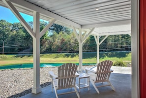 Un porche cubierto con sillas Adirondack y vista a una piscina verde.