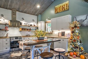 Een keuken met witte kastjes, een houten eiland met krukken, een kerstboom en een oud bord aan de muur.