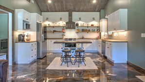 Una cocina moderna con armarios blancos, una isla central con taburetes y un piso de mármol pulido.