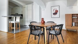 A modern kitchen with white cabinets, a dining area with a round wooden table and black chairs, and a wooden cabinet with a shelf.