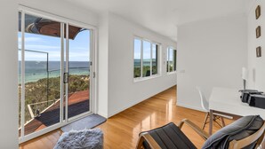 Una habitación moderna con piso de madera, un escritorio blanco, una silla y vistas al mar a través de amplios ventanales.