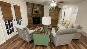 Ein Wohnzimmer mit zwei grauen Sesseln, einem grünen Couchtisch, einem Kamin und einem Deckenventilator.