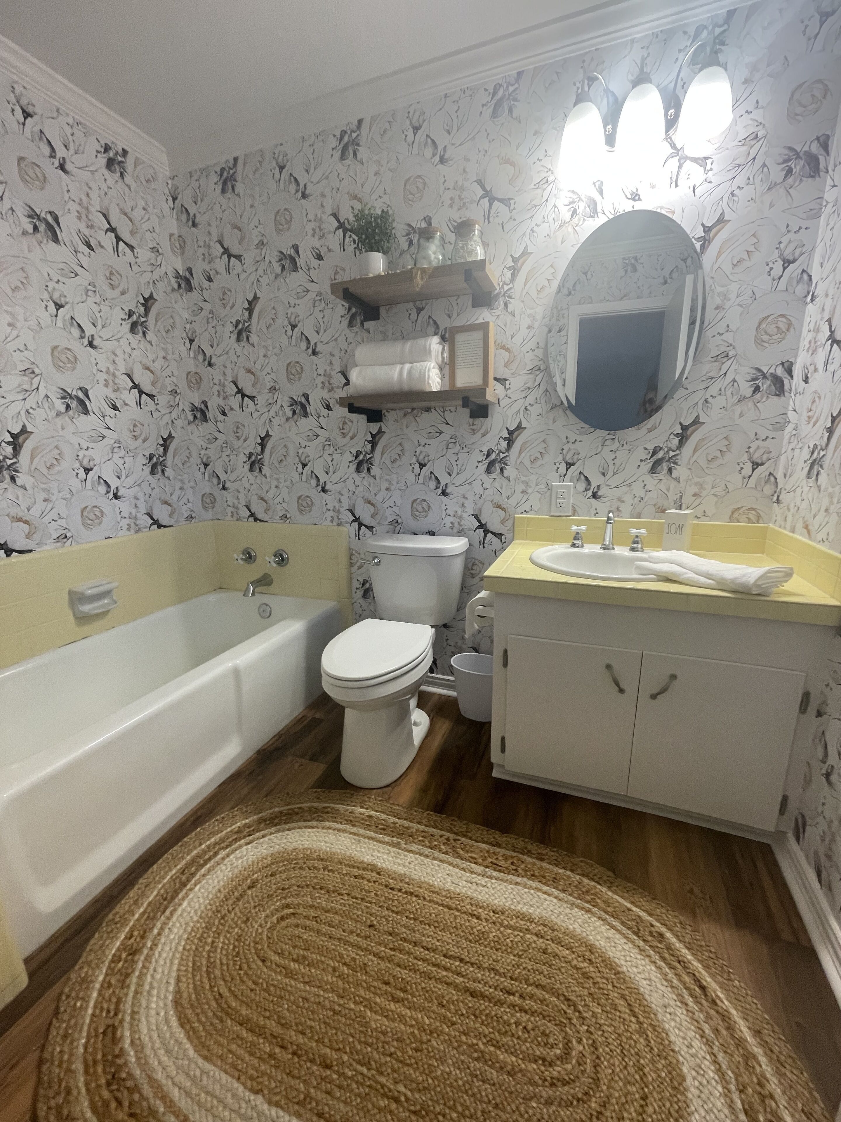 Un baño con bañera, inodoro y lavabo. Hay un espejo sobre el lavabo y una repisa con toallas.