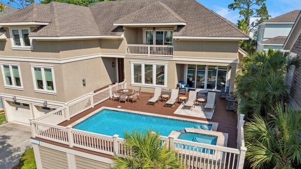 Une maison à deux étages avec une piscine, du mobilier d’extérieur et un balcon.