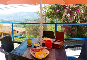 Ein Esstisch mit Frühstücksangeboten und Blick auf Berge und Grün.