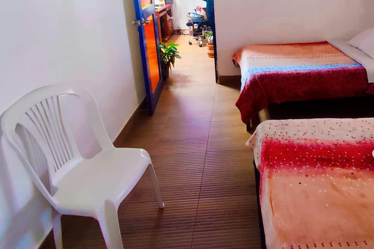 A hotel room with two beds, a white plastic chair, and a small desk with a computer.