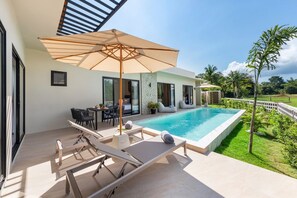 A modern outdoor pool area with lounge chairs, a table, and an umbrella. - Sereniwood 2 - 3 Bedroom Pool Villa (Koh Samui)