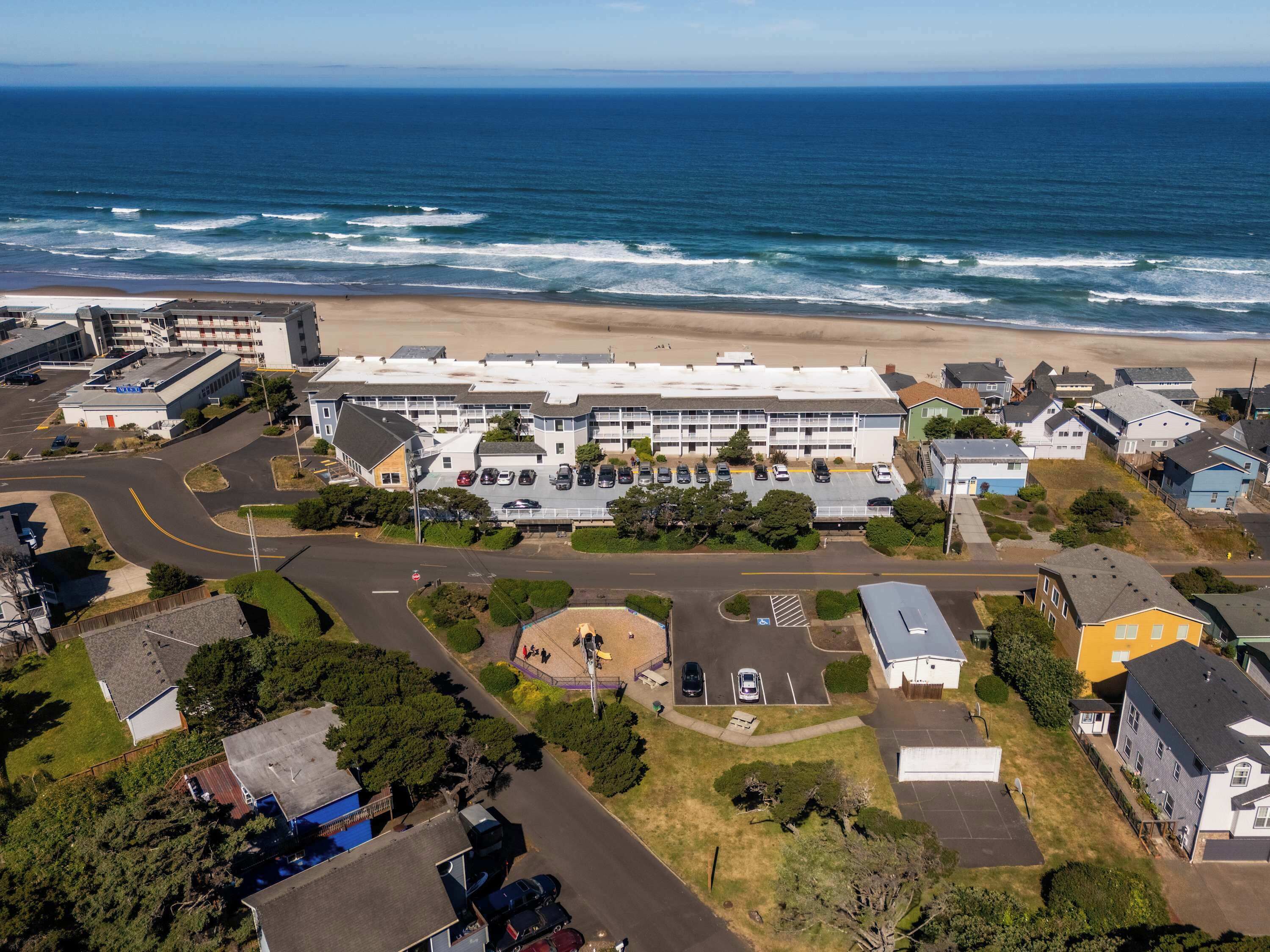 Vista aérea de uma área residencial costeira, com um grande complexo de edifícios, estacionamentos e uma praia ao fundo.