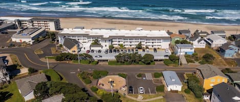 Vista aérea de uma área residencial costeira, com um grande complexo de edifícios, estacionamentos e uma praia ao fundo.