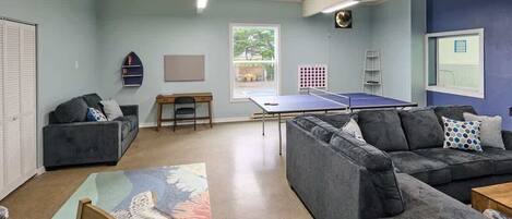 A room with two grey sofas, a ping pong table, a small table, and a chair.