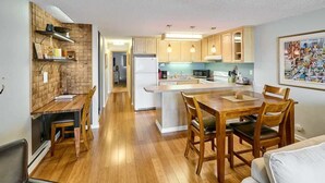 Una cocina compacta con armarios de madera, una isla central y una zona de comedor con mesa y sillas.