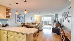 Una cocina moderna con zona de comedor, armarios de madera, luces colgantes y vistas al balcón.