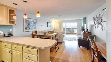 A modern kitchen with a dining area, wooden cabinets, pendant lights, and a view to the balcony.