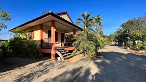 A two-story house with a red and yellow facade, a porch with a wooden railing, and a concrete driveway. - Chatchawan Resort (Uttaradit)
