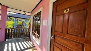 A wooden door with a number plate marked 'B2', a balcony with a wooden railing, and a view of greenery outside. - Chatchawan Resort (Uttaradit)