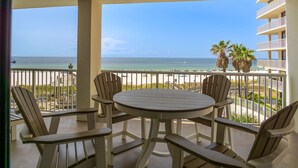 A balcony with a round table and chairs, overlooking a beach with palm trees and a clear sky. - Summer House 306A from ALBVR -- Completely Renovated & Better Than Ever! (Orange Beach)