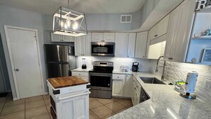 A kitchen with white cabinets, stainless steel appliances, a wooden cutting board, and a marble countertop. - Summer House 306A from ALBVR -- Completely Renovated & Better Than Ever! (Orange Beach)