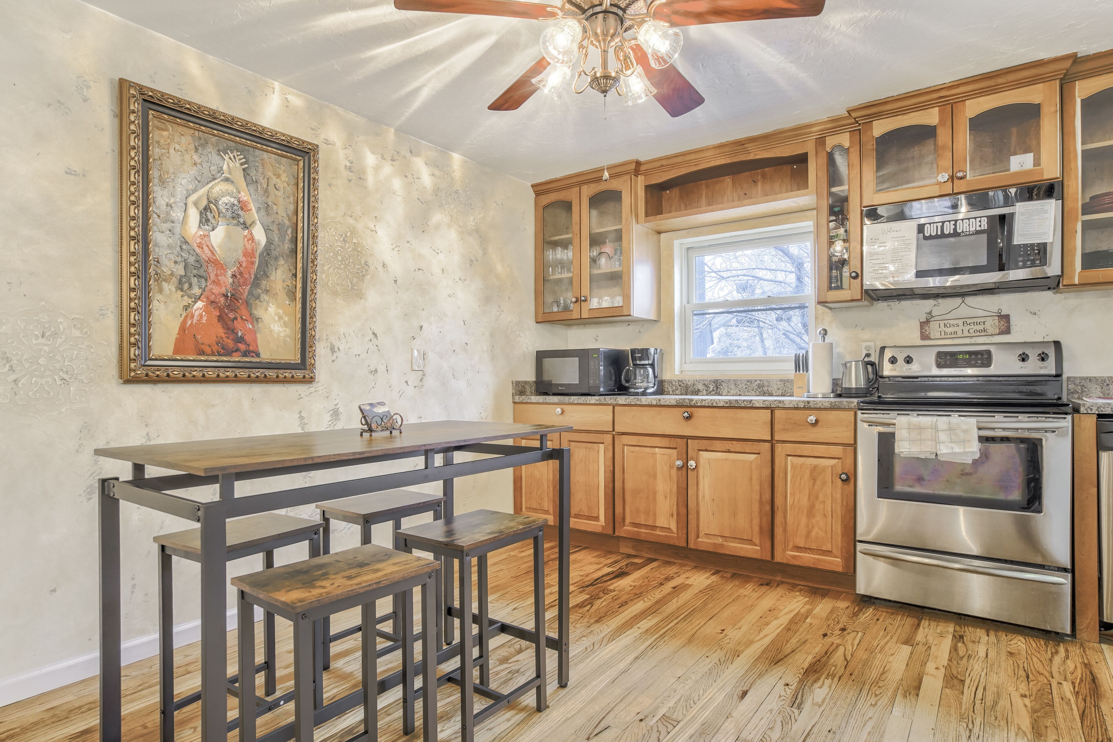 A kitchen with wooden cabinets, stainless steel appliances, a dining table with stools, and a ceiling fan.